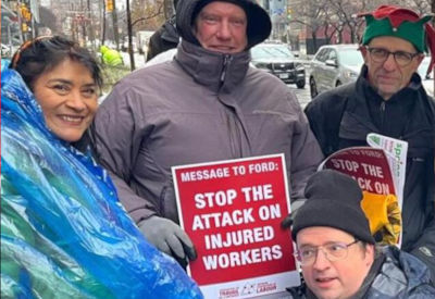 Four people participating in a protest against policy changes affecting injured workers. One holds a red sign that reads, 'Message to Ford: Stop the Attack on Injured Workers.' A wintery city street is in the background.